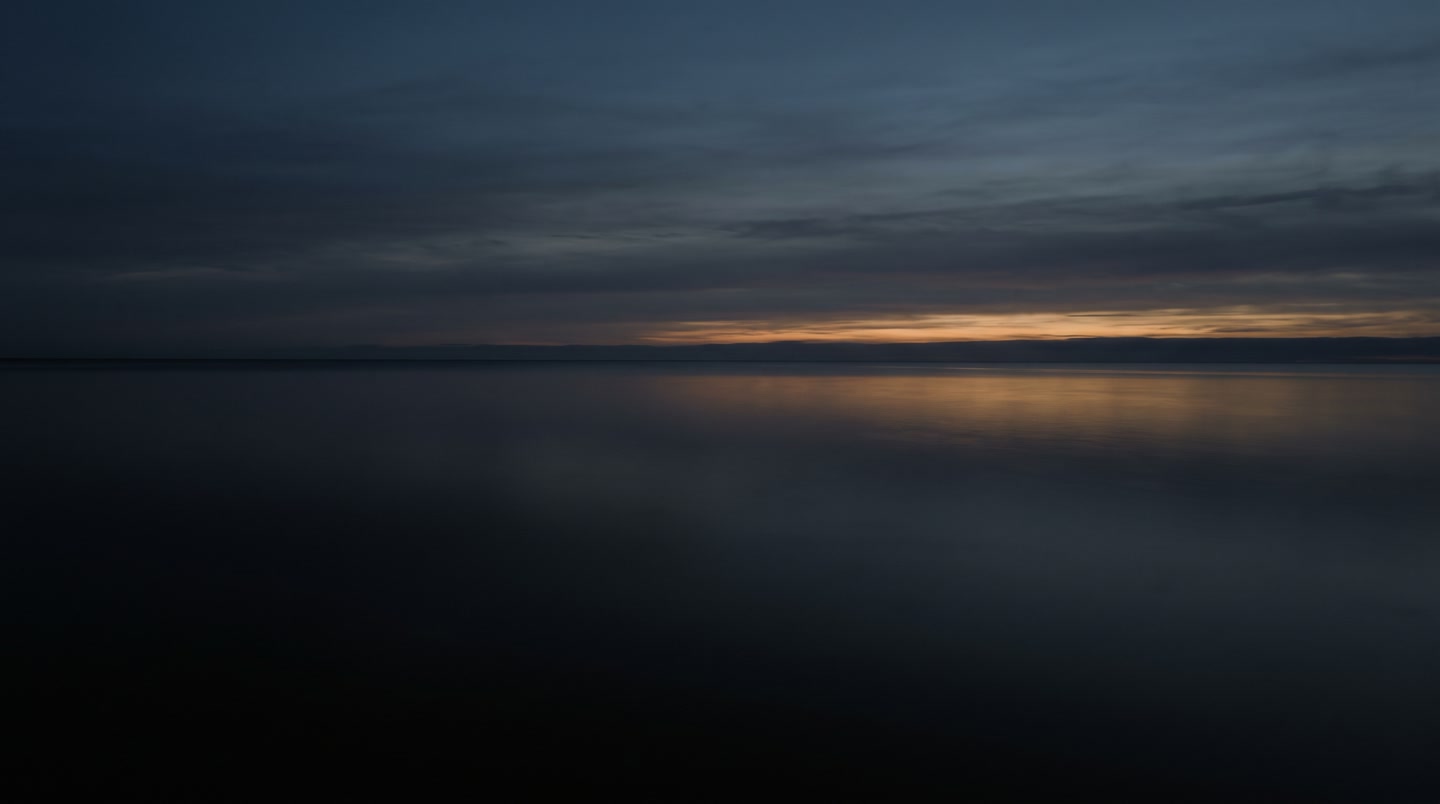 A calm sea at dusk; a warm band of light on the horizon.